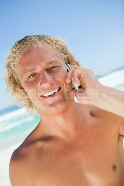 Stock photo: Smiling blonde man looking at the camera while calling with his cellphone