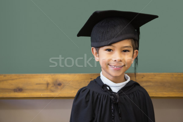 Cute pupil in graduation robe smiling at camera in classroom Stock photo © wavebreak_media