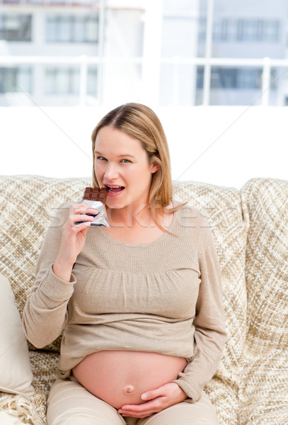 Pretty future mom eating a chocolate bar sitting on the sofa at home Stock photo © wavebreak_media