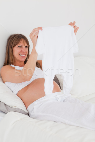 Attractive pregnant female showing a little white pyjama while lying on a bed in her apartment Stock photo © wavebreak_media
