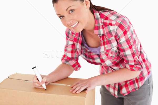 Portrait of an attractive woman writing on cardboard boxes with a marker while standing against a wh Stock photo © wavebreak_media