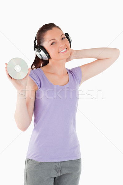 Stock photo: Pretty woman with headphones holding a CD while standing against a white background