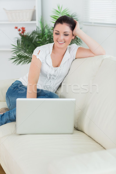 Stock photo: Woman sitting on the couch in a living room and smiling while using a laptop