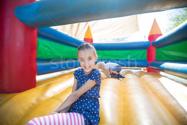 Happy girl sitting on bouncy castle while brother playing in background Stock photo © wavebreak_media