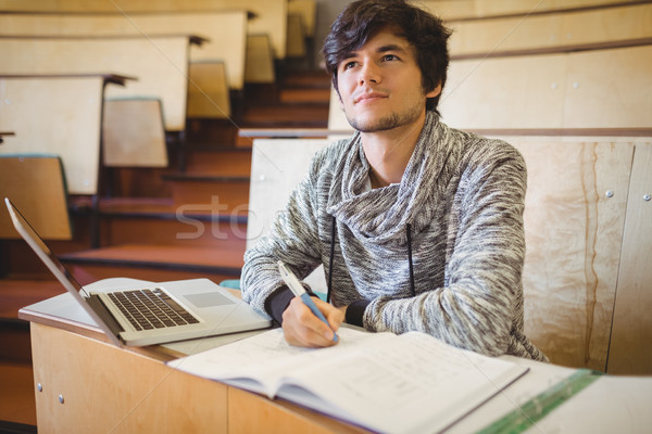 Thoughtful young student sitting at desk with book and laptop Stock photo © wavebreak_media
