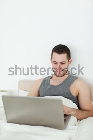 ストックフォト: 濃縮された · 男 · ラップトップを使用して · ベッド · コンピュータ · 笑顔