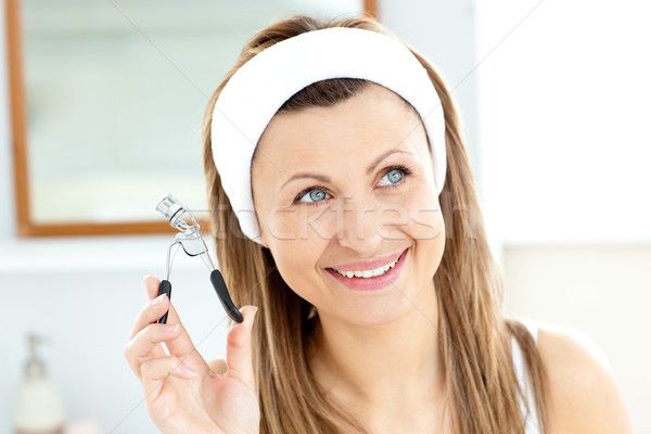 Smiling woman holding an eyelash curler looking at the camera in the bathroom at home Stock photo © wavebreak_media