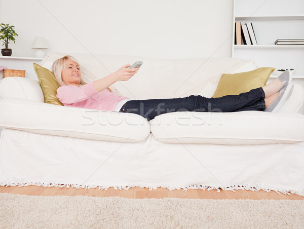 Pretty blonde woman watching tv while lying on a sofa in the living room Stock photo © wavebreak_media