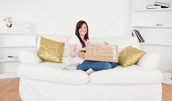 Beautiful red-haired female opening a carboard box while sitting on a sofa in the living room Stock photo © wavebreak_media