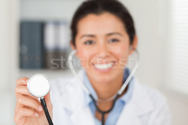 Stock photo: Attractive female doctor using a stethoscope while looking at the camera in her office