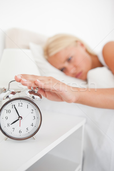 Portrait of an unhappy woman switching off her alarmclock in her bedroom Stock photo © wavebreak_media