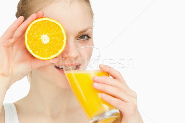 Woman placing an orange on her eye while drinking against white background Stock photo © wavebreak_media