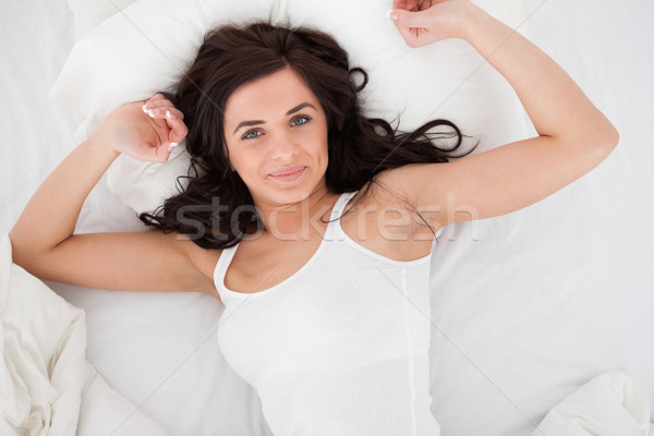 Stock photo: Peaceful brunette woman stretching her body while lying in a bedroom