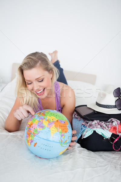 Student with a suitcase pointing on a globe while lying on her bed Stock photo © wavebreak_media