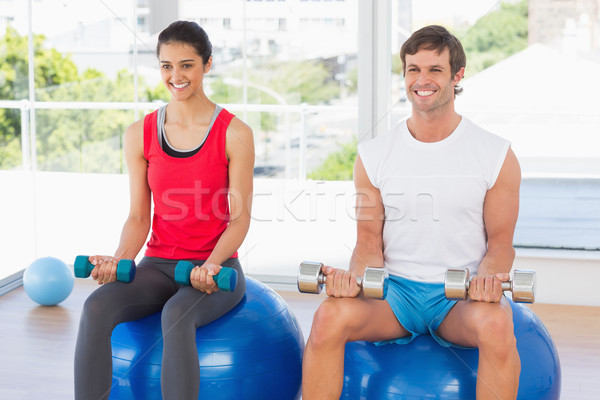 Stock photo: Couple lifting dumbbells while sitting on fitness balls in gym