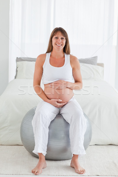 Pretty pregnant female caressing her belly while sitting on a gym ball in her bedroom Stock photo © wavebreak_media