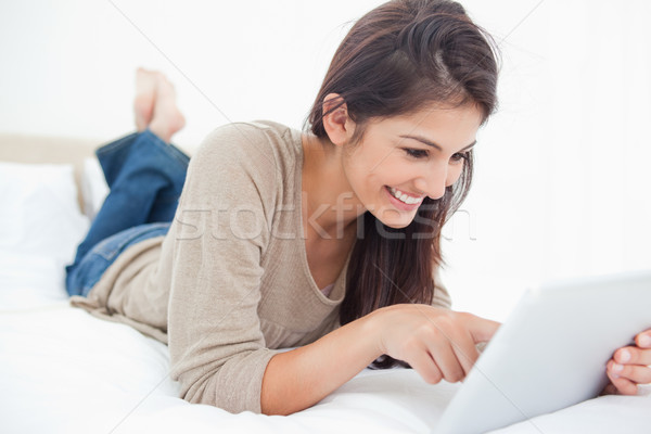 A smiling woman lies on the bed scrolling through her tablet. Stock photo © wavebreak_media