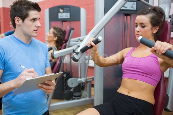 Trainer noting progress of woman using weights machine Stock photo © wavebreak_media