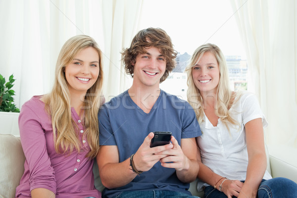 Three friends sitting together looking at the camera with  a mobile phone Stock photo © wavebreak_media