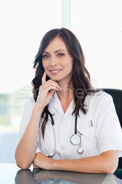 Young doctor sitting at the desk wihile putting her finger against her cheek Stock photo © wavebreak_media