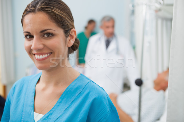 Smiling nurse in hospital room with doctor, patient and other nurse in background Stock photo © wavebreak_media