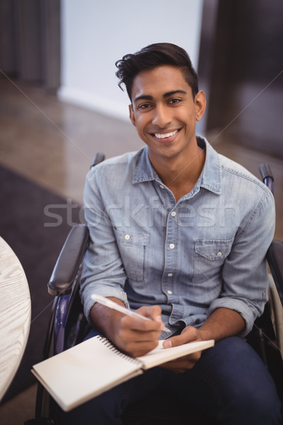 Smiling businessman writing in book while sitting on wheelchair Stock photo © wavebreak_media