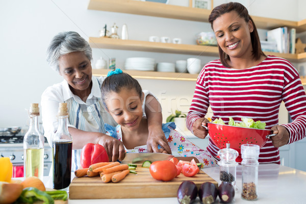 Stock photo: Grandmother assisting granddaughter to chop vegetables in kitchen