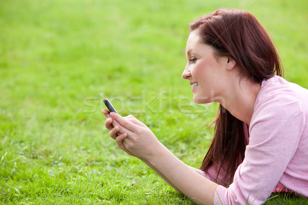 Stock photo: Delighted young woman writing a message on her phone sitting on the grass