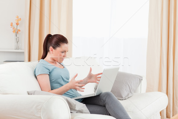 Stock photo: Charming upset woman gambling with her computer while sitting on a sofa in the living room