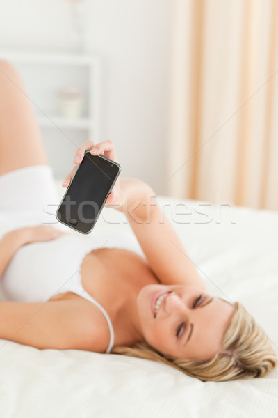 Portrait of a cute blonde woman showing her phone while lying on her bed Stock photo © wavebreak_media