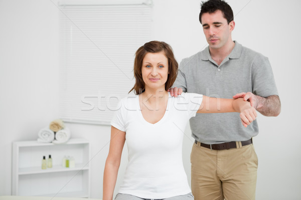 Stock photo: Doctor examining the shoulder of his patient while holding his arm in a room
