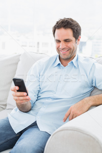 Cheerful man sitting on the couch sending a text with smartphone Stock photo © wavebreak_media