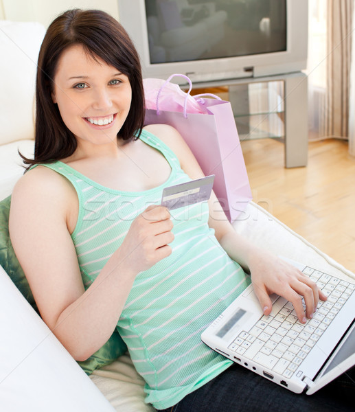 Stock photo: Glowing young woman holdign a card using her laptop