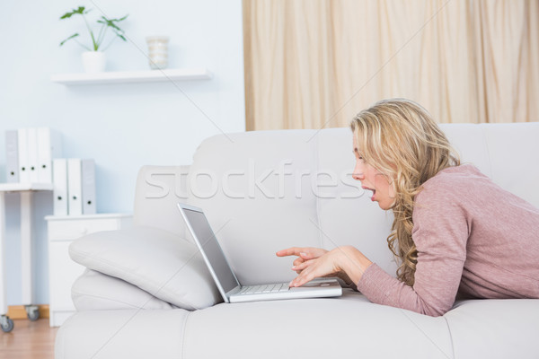 Surprised blonde lying on couch using laptop Stock photo © wavebreak_media