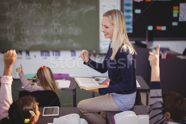 Schoolkids raising their hands while teacher teaching in classroom Stock photo © wavebreak_media