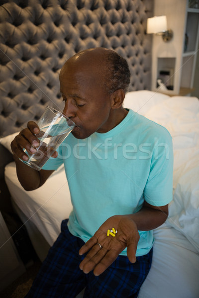Senior man holding medicine while drinking water in bedroom Stock photo © wavebreak_media