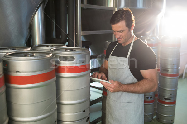 Stock photo: Worker using digital tablet on notepad while standing by kegs