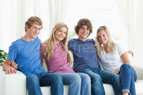 A group of friends look at the camera and smile as they sit on the couch together Stock photo © wavebreak_media