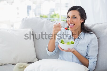 Smiling beautiful brunette relaxing on the couch and eating sala Stock photo © wavebreak_media