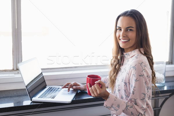 Portrait of smiling businesswoman holding coffee cup while working on laptop Stock photo © wavebreak_media