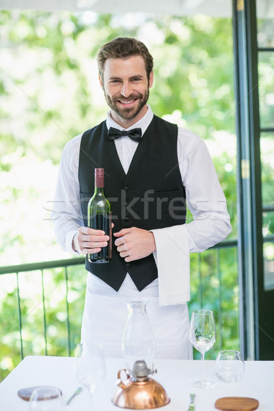 Stock photo: Male waiter holding bottle of wine