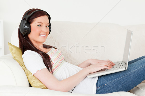 Stock photo: Good looking red-haired woman listening to music with headphones while relaxing with her laptop in t
