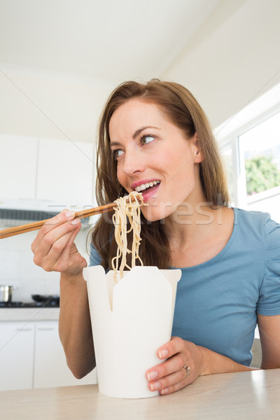 Stock photo: Smiling young woman eating noodles in kitchen