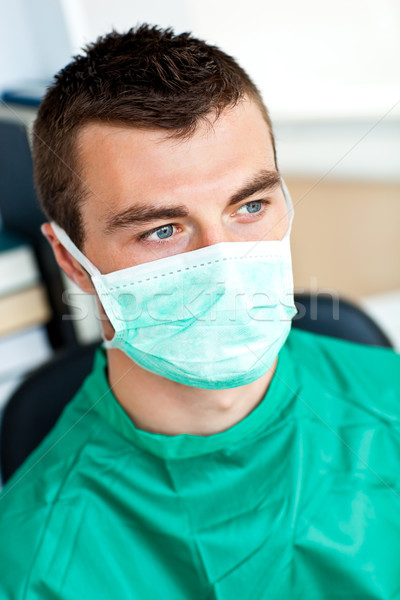 Stock photo: Serious male surgeon with mask and scrubs sitting in his office