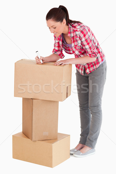 Gorgeous woman writing on cardboard boxes with a marker while standing against a white background Stock photo © wavebreak_media