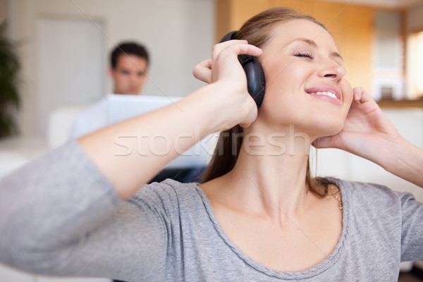 Stock photo: Young woman enjoying music with man sitting behind her on the sofa