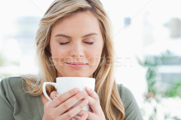 Stock photo: A woman with a soft smile and closed eyes, smelling the aroma from her cup in front of her.