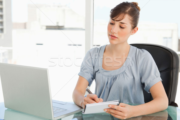 A business woman with a notepad takes notes down from her laptop Stock photo © wavebreak_media