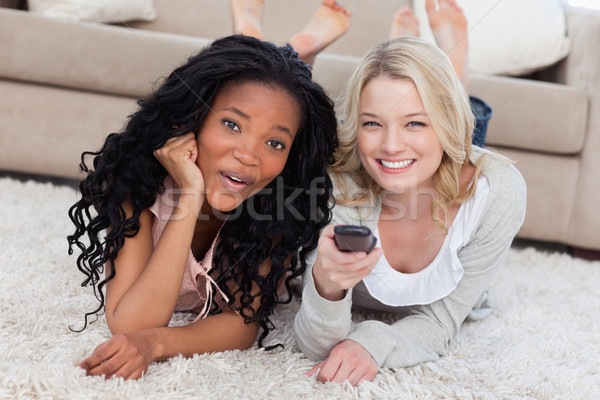 Two women are smiling at the camera and lying on the ground with a TV remote Stock photo © wavebreak_media