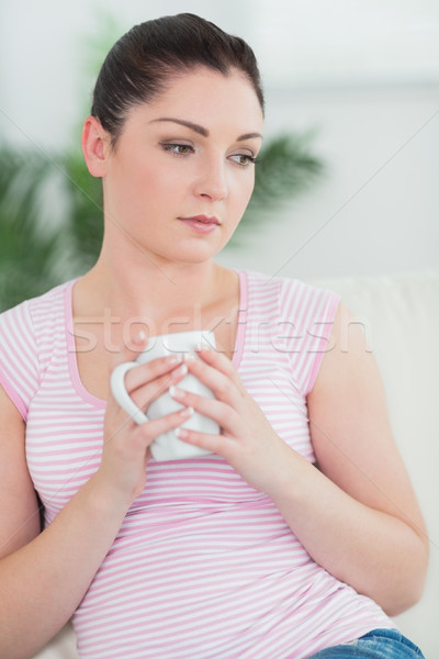 Thoughtfully woman sitting on the couch in a living room and holding a cup Stock photo © wavebreak_media